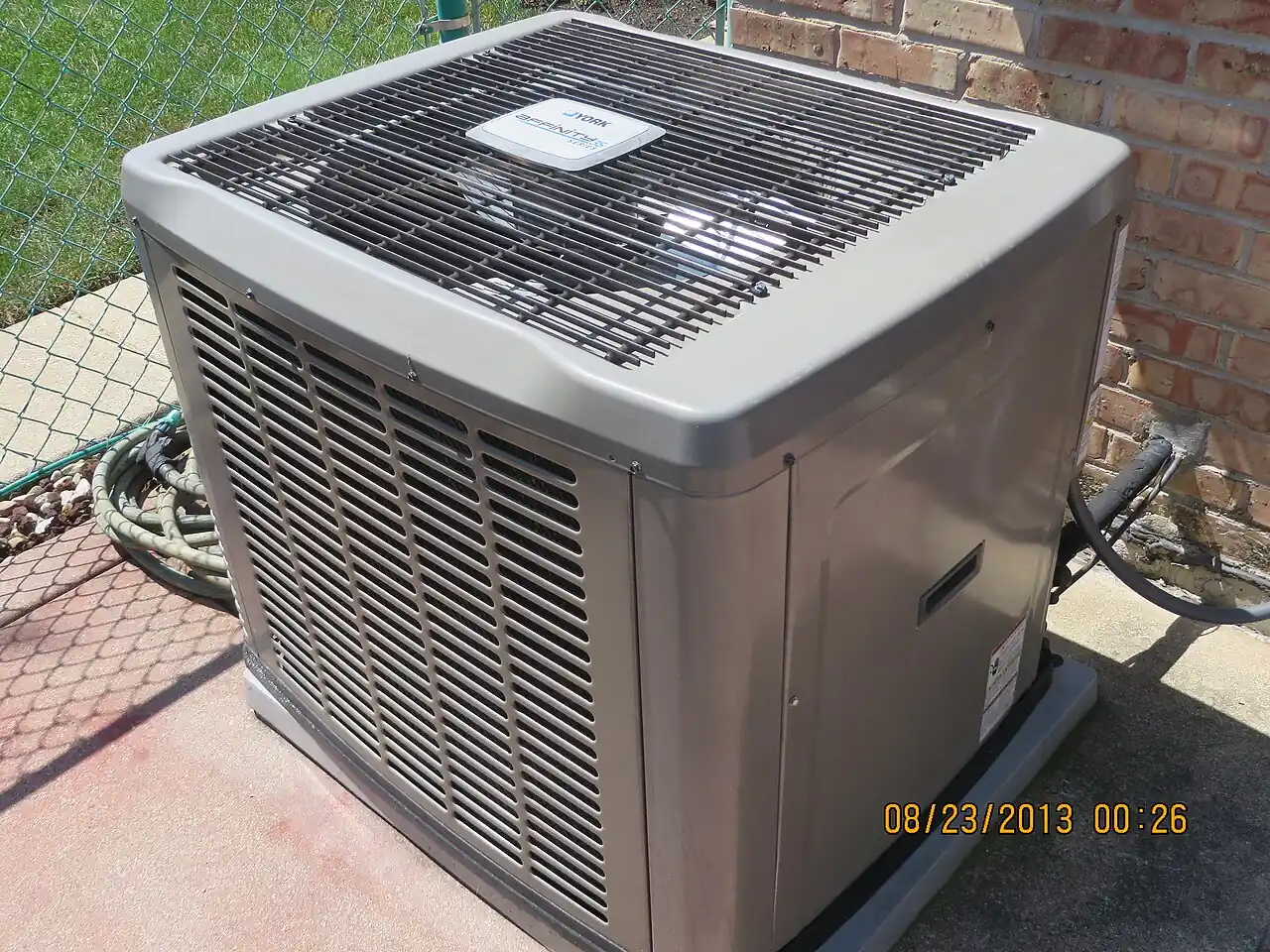 A residential central air conditioning condenser unit on a concrete pad beside a house.