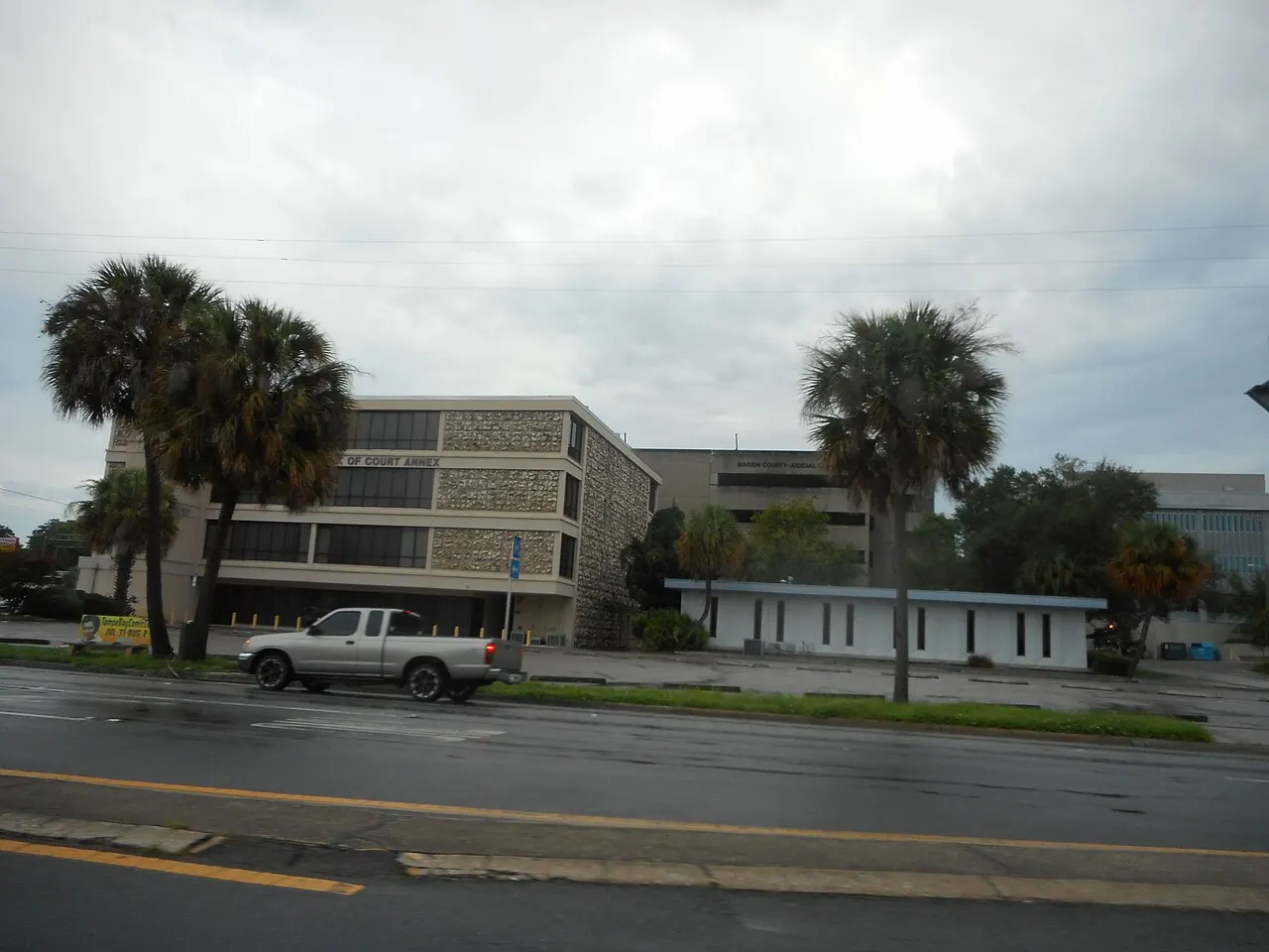 The Marion County Court Building in Ocala, seen from the road behind trees.