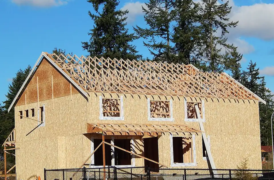 A two-storey house under construction, sheathed in structural panels with its roof trusses set and no cladding yet.