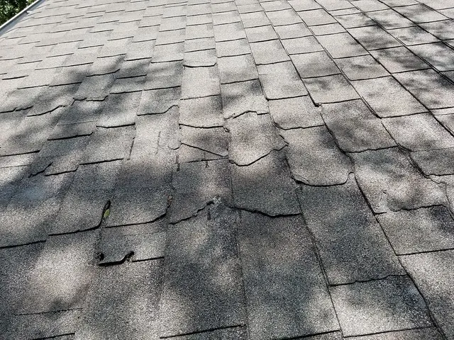 A close view of an asphalt shingle roof with shingles lifted, curled and torn after a storm.