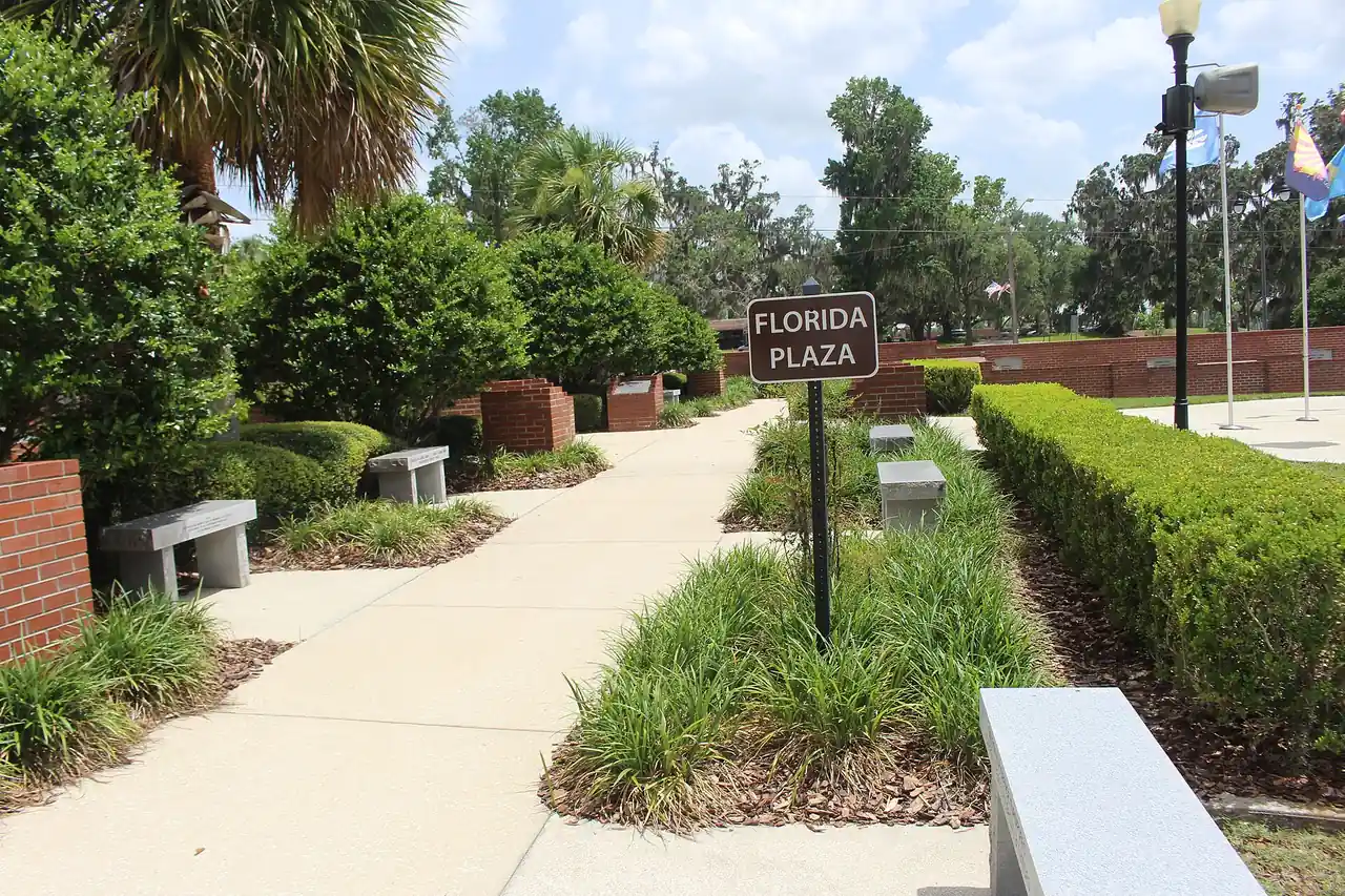 A brick-walled memorial plaza in Ocala with clipped hedges, benches and a signpost reading Florida Plaza.
