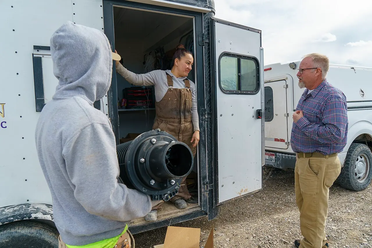 Fibre-optic cable being installed along a rural roadside, spooled on a trailer beside an open trench.